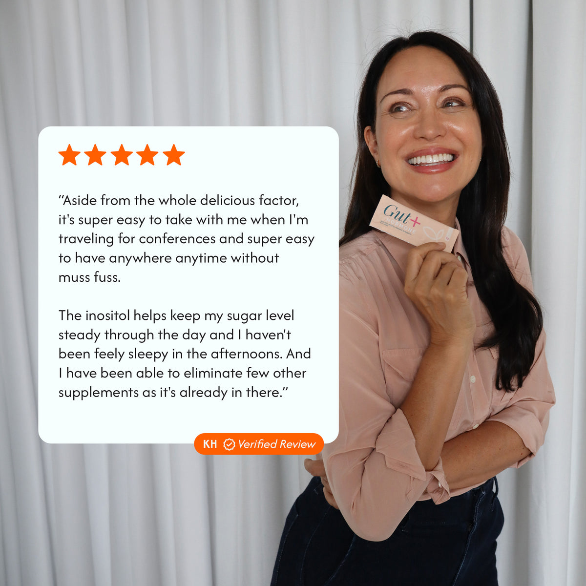 A woman smiling and holding a pink GUT+ supplement box, with a large white review card overlaid on the left showing a five-star quote and orange text. The background is a soft white curtain.