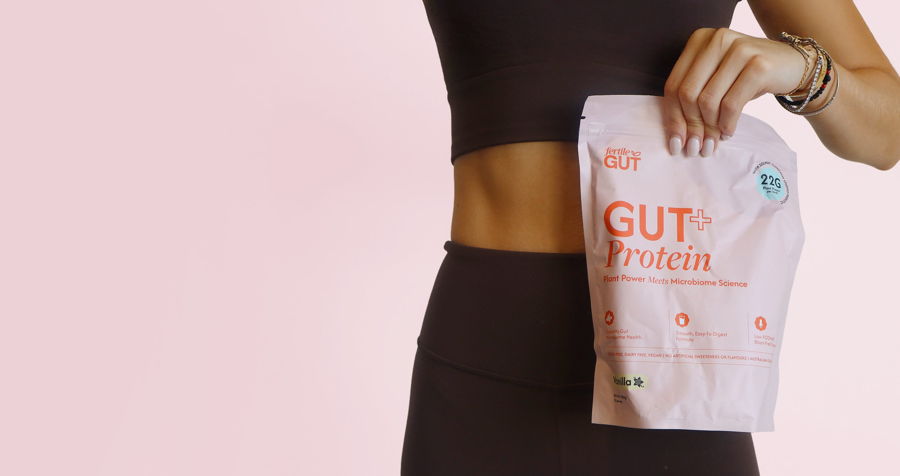 Person holding a 'GUT + Protein' package against a pink background